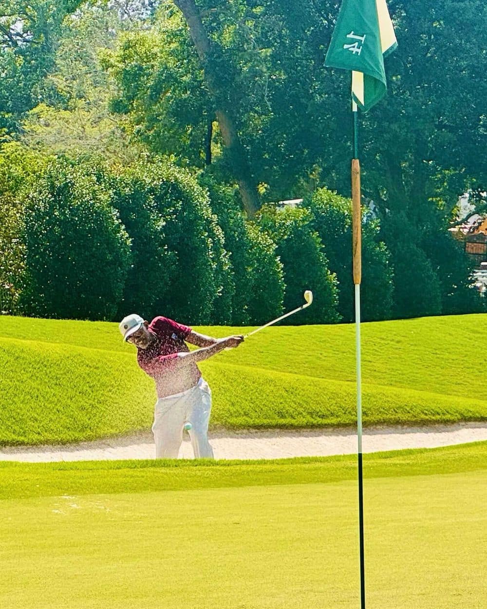Jeffrey playing a bunker shot toward the pin on a sunlit green